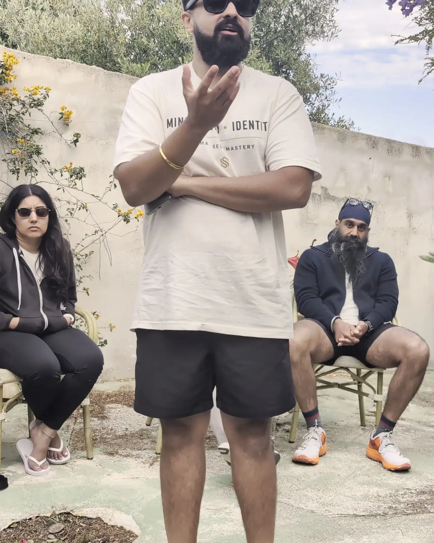 Sukh standing in the villa garden, talking with his hands, the group in chairs around him