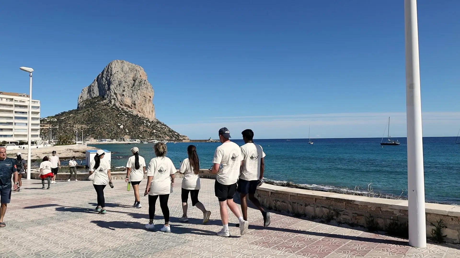 The group in matching T-shirts walking the seafront, the rock ahead