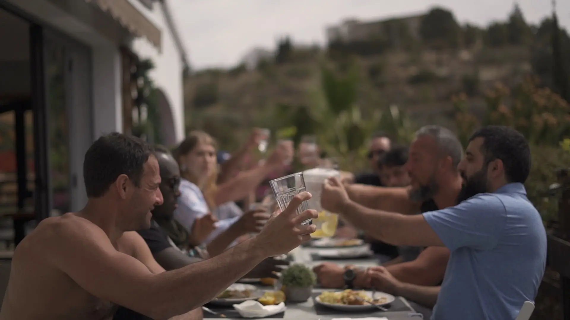 A long table outdoors, the whole group raising glasses over lunch